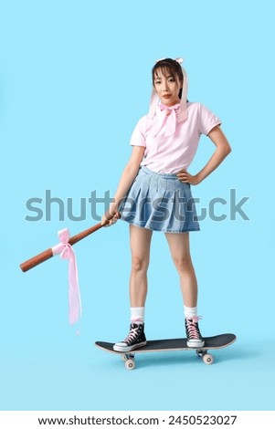 Young Asian woman with pink bows and bat on skateboard against blue background
