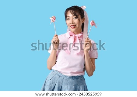 Young Asian woman with pink bows and lollipops on blue background