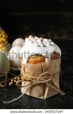 Sweet Easter cake, mimosa flowers and holder with eggs on black background Royalty-Free Stock Photo #2450527249