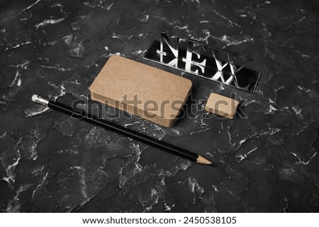 Blank kraft business cards, pencil, eraser and metal plate with the inscription NEW on black plaster background. Branding identity template.
