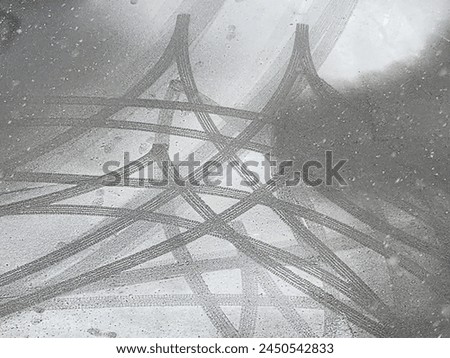 The intricate and captivating patterns formed by the black tire skid marks on the snow-covered road surface create a visually striking and unique design that catches the eye.