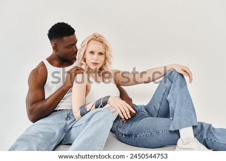 A young interracial couple sitting together, exuding love and connection, on a grey studio background.