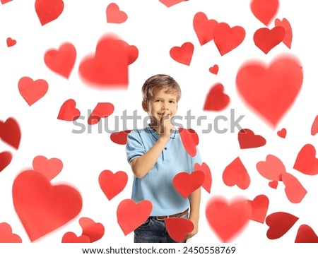 Cute little boy gesutring silence with finger under red hearts isolated on white background