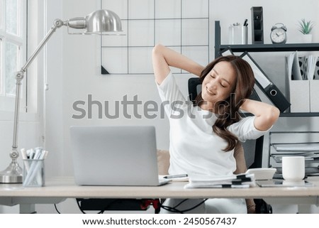 Relaxed professional woman takes a break to stretch at her workstation, signaling a moment of well-deserved rest in her busy day. Royalty-Free Stock Photo #2450567437
