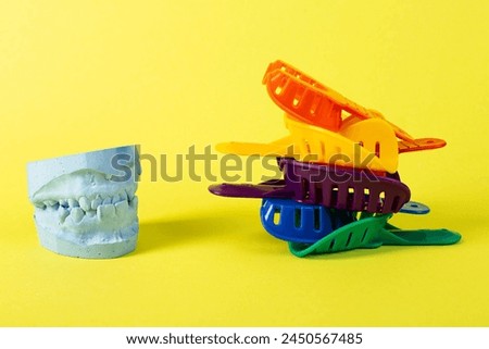 Blue plaster cast of a dental jaw and a dental tray for an impression of a dental jaw on a yellow background. The concept of orthodontics in dentistry, the manufacture of dentures and crowns.  Royalty-Free Stock Photo #2450567485