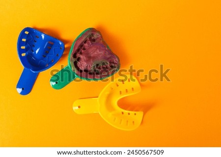 Multi-colored dental spoons for taking an impression of the dental jaw on a orange background. Making an impression of the jaw for braces and dental prosthetics. Copy space for text Royalty-Free Stock Photo #2450567509