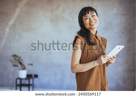 Image of an asian businesswoman with confidence and creativity. Using a tablet at the office. Female professional at office with digital tablet. Businesswoman in smart casuals standing in office.