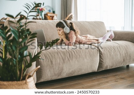 A sweet little girl, aged 5-6 years old, wearing headphones as she watching a laptop screen, fully engaged in her digital entertainment Royalty-Free Stock Photo #2450570233