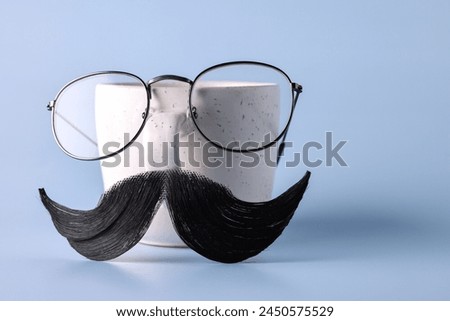 Man's face made of artificial mustache, glasses and cup on light blue background. Space for text