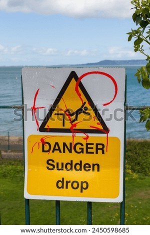 Danger, Sudden drop road sign against green grass and sea background on a cloudy day