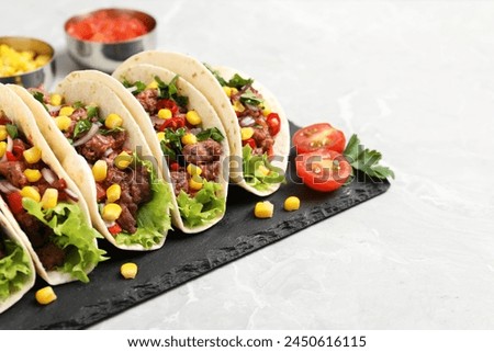 Delicious tacos with meat and vegetables on light gray marble table, closeup