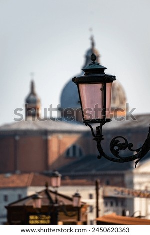 This photo features a classic ornate lamp post in Venice, Italy. The lamp post is topped with a decorative globe and its  black, wrought iron  curves add a touch of old-world charm to any space.