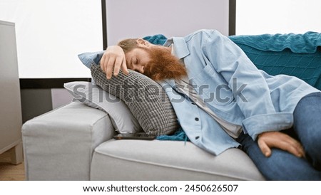 Exhausted young irish man with redhead beard finds comfort relaxing on cozy sofa, deeply sleeping at home in the living room, relishing the relaxation of a well-deserved rest Royalty-Free Stock Photo #2450626507