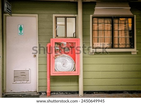 This photo was taken from the front, showing a white toilet door, with a fire hose and fire cupboard next to the door