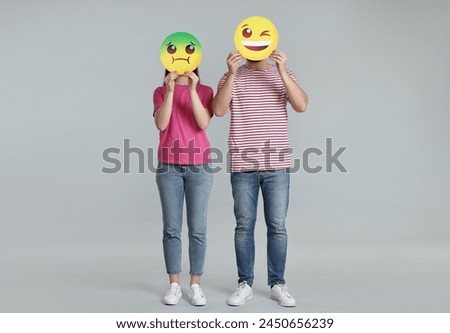 People covering faces with emoticons on grey background