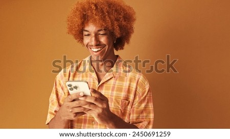 Cheerful stylish curly guy uses a mobile phone isolated on brown background in the studio