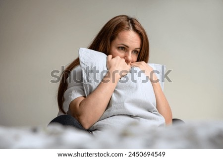 Lonely woman sits on the bed in bedroom and hugging pillow. Depressed woman with blank expression. Royalty-Free Stock Photo #2450694549
