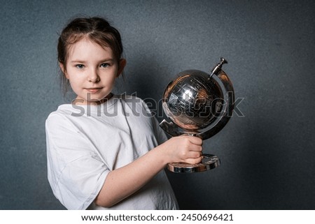 Cute little girl in white t-shirt holding a globe and looking into the frame. High quality photo