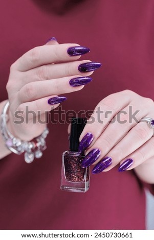 Woman hand with long nails and a bottle of plum purple nail polish