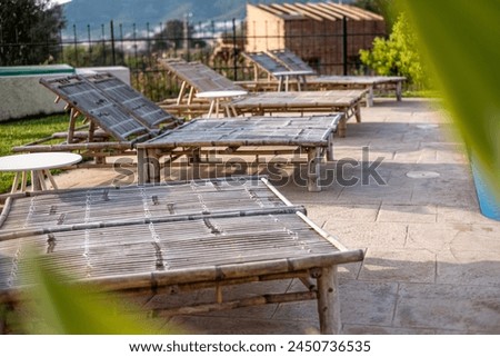 Bamboo sunbeds lined up by the pool, a hint of greenery in the foreground, serene holiday vibe for relaxation. High quality photo