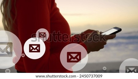 Image of mail icons over midsection of biracial woman using smartphone at beach. global connections, social media, technology and digital interface concept digitally generated image.