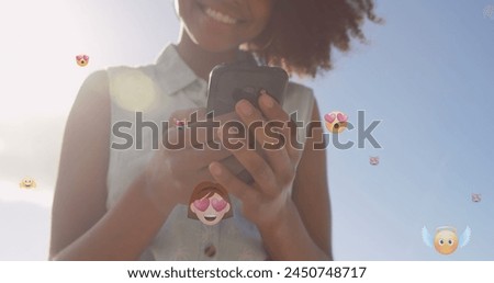 Image of emoticons over midsection of biracial woman using smartphone outdoors. global connections, social media, technology and digital interface concept digitally generated image.