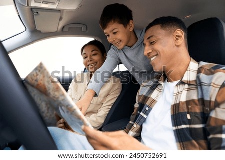 Road trip adventure. Happy family of three with boy looking at map sitting in car and choosing destination. Travel by automobile Royalty-Free Stock Photo #2450752691