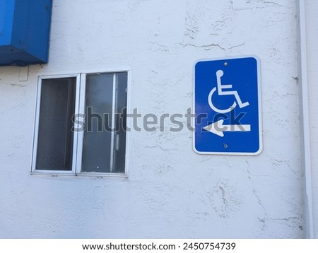 A blue and white handicap sign has an arrow that points directly into a sliding window on the wall.        