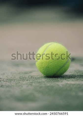 Close-up of a bright yellow tennis ball on a textured green court with net in the background