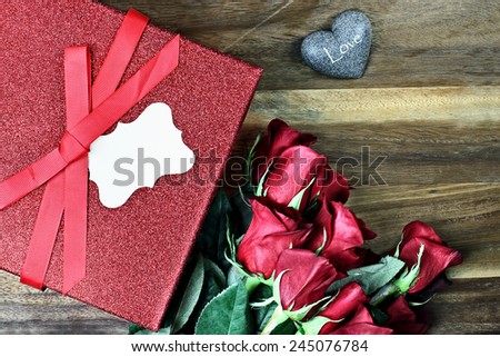Gift box with long stem red roses and blank card over an old wooden background with room for copyspace.