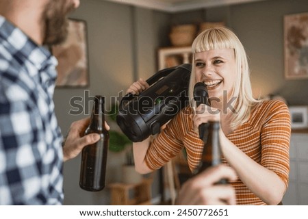 Adult woman caucasian sign karaoke on microphone and man hold bottle of beer at home