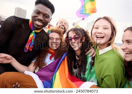A happy crowd of LGBT people wearing colorful smiling for a picture with a rainbow flag at a fun pride day parade event. They exude leisure and travel vibes. Community and friendship