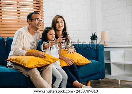 Family time is filled with joy and togetherness as an Asian family watches TV movies on the sofa in their grooved modern house. The father mother son and daughter are all smiles.