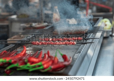 Delicious Adana kebabs are grilling on a barbecue with smoke and red peppers, close up, outdoor photography