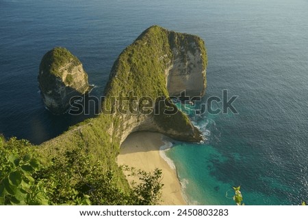 Under the vast expanse of a blue sky, the Kelingking Beach reveals its captivating allure with steep cliffs rising majestically along the coastline. Sparkling white sands glisten under the radiant sun Royalty-Free Stock Photo #2450803283