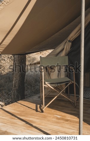 A vertical picture of a directors chair in front of a safari tent in South Africa. Warm colours of a safari interior design. Sitting area in front of a tent during camping. Kaki green chair. 