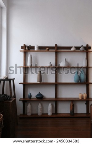 A wooden shelf with colorful ceramic vases with different shapes on it with white wall background