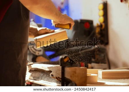 Craftsperson at workbench using manual sandpaper to sander lumber block, assembling furniture in woodworking shop. Carpenter smoothing piece of wood, enjoying diy hobby, close up Royalty-Free Stock Photo #2450842417