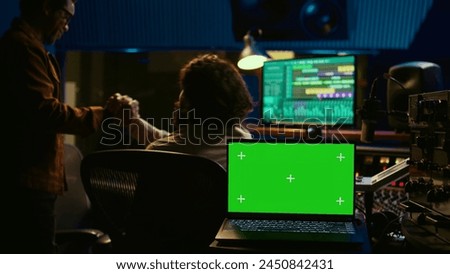 Artist and sound designer working as a team to produce new tracks, greenscreen laptop. Musician and audio technician collaborating on music, mixing on audio console with motorized faders. Camera B.