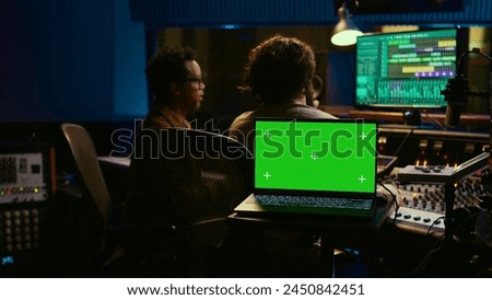 Team of artist and music producer work with mockup display, processing and mixing sounds in professional studio control room. Experts producing tracks by using technical equipment. Camera B.