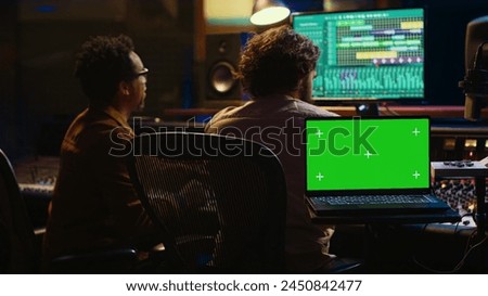 Team of artist and music producer work with mockup display, processing and mixing sounds in professional studio control room. Experts producing tracks by using technical equipment. Camera A.