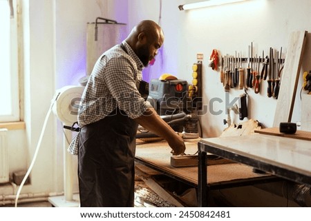 Craftsperson at workbench selecting high quality wood materials for commissioned project. African american woodworking professional doing quality assurance on timber piece Royalty-Free Stock Photo #2450842481