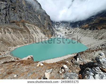 A turquoise glacial lake nestled in the Himalayan mountains of Nepal, with cloudy skies above.  Royalty-Free Stock Photo #2450855175