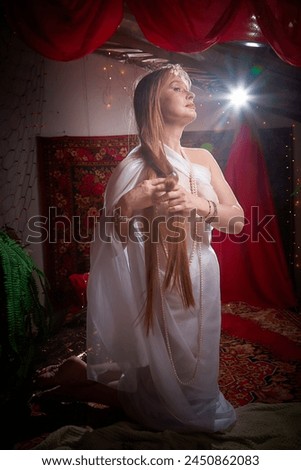 Beautiful European girl looking like Arab woman in red room with rich fabrics and carpets in sultan harem. Photo shoot of an oriental style odalisque. A model poses in sari as an indian woman in india