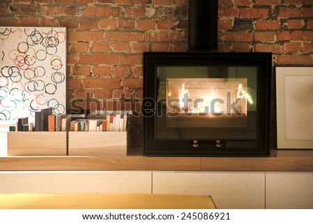 Fragment of interior loft. Burning fireplace. Picture Frames and photos. Books in wooden boxes. Without plaster wall of red brick.