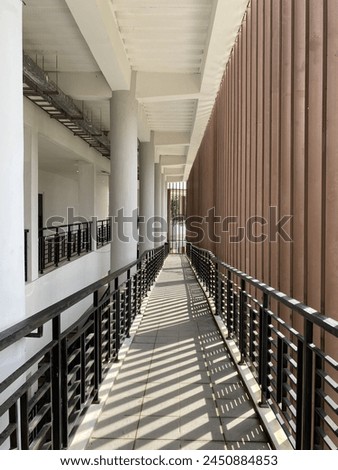 hallway in a university with a modern look, on the right there is a brown grid and on the left there are several round white pillars with the hallway floor using gray ceramic