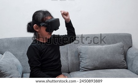 A young girl is playing a video game with a virtual reality headset on. She is pointing at something on the screen. Happy with her VR