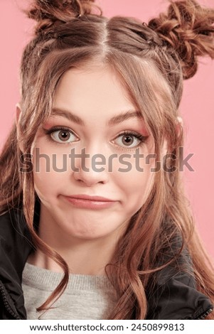 Closeup of a cute teenage girl, dressed in casual clothes, with cute hair bumps on her head and wavy hair. Pink background. Youth style.