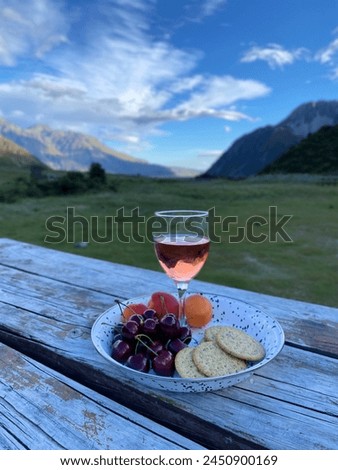 A glass of rose wine, fresh fruits and cracker in the plate on the wooden table with beautiful mountain views at the background 