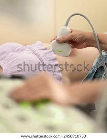Ultrasound of woman's abdominal cavity. Ultrasound screening of digestive system. Ultrasound sensor in hand of female doctor. Appointment with ultrasound specialist. Side view. Soft focus. Royalty-Free Stock Photo #2450910753